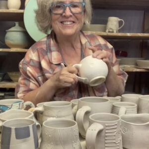 Cori Sandler at the wheel with many greenware mugs in the decorating process